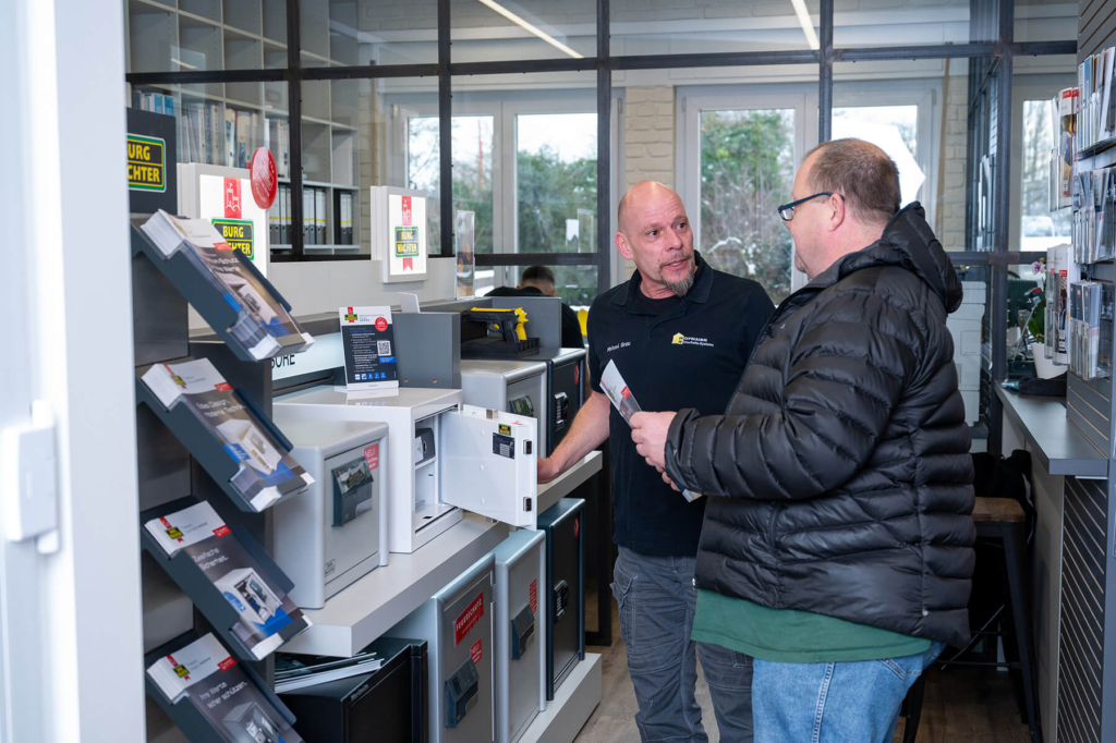Kunde berät sich mit einem Verkäufer in einem Geschäft für Sicherheitstechnik vor einem Regal mit Safes.