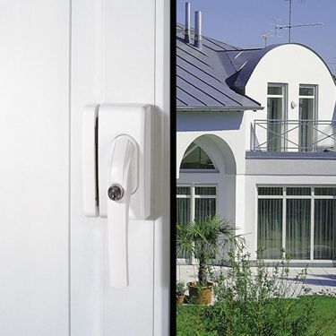 Fenstergriff an einem weißen Fenster mit Blick auf ein modernes Haus und grünen Pflanzen im Garten.